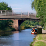 The bridge at Broad Cut- bridge over a canal with a canal boat and greenery on the side